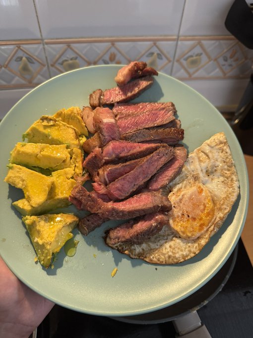 A green plate held up showing sliced medium-rare steak, yellow rice or mashed potatoes, and a fried egg.