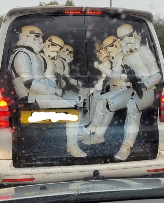 A white van's rear doors feature a large vinyl decal depicting two groups of Star Wars stormtroopers sitting across from each other.