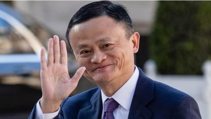 A portrait of Jack Ma, the founder of Alibaba, smiling and waving his hand while wearing a dark suit and purple tie.
