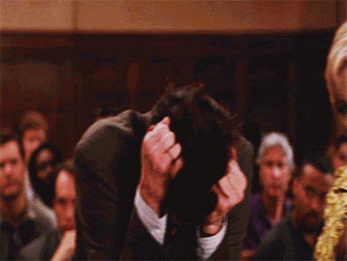 The image shows a man sitting in front of an audience, with his head down and hands covering his face. He appears to be in distress or sadness. The surrounding crowd consists of people who are watching him closely. There is also a woman wearing a gold necklace visible in the scene.