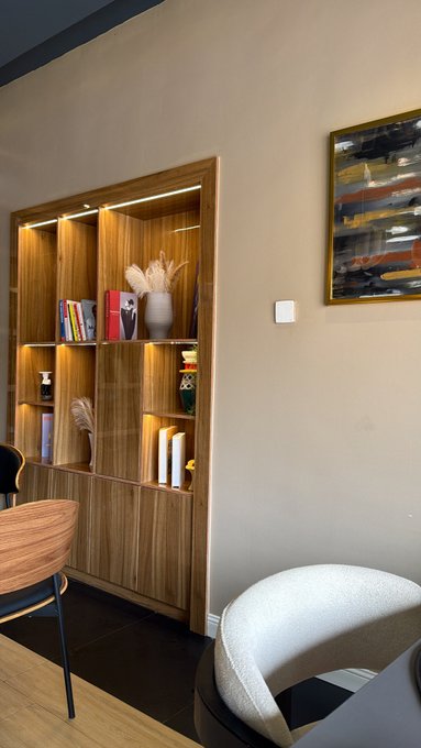 Interior view of a modern room featuring a built-in wooden display shelf with LED lighting, decorative items, and an abstract painting on the adjacent wall.