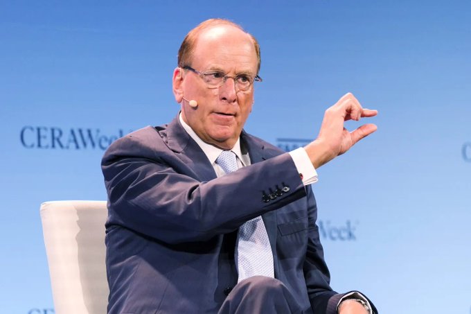 A man in a dark suit and glasses speaks and gestures with his hand while seated on a panel at a CERAWeek event.