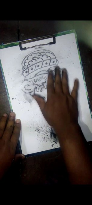 A photograph of a person's hands smudging a charcoal or pencil drawing of a brain on a clipboard.