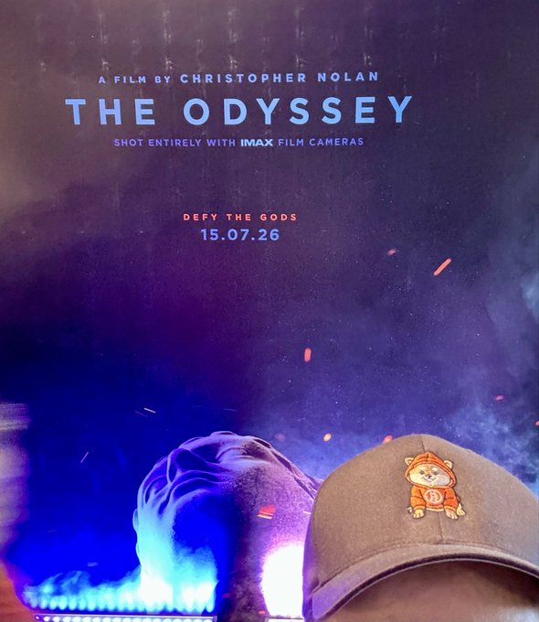 A promotional poster for Christopher Nolan's 'The Odyssey' film shot entirely with IMAX film cameras, release date 15.07.26, with a person wearing a cap visible in the foreground against a smoky blue background.