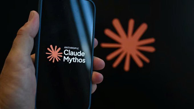 A hand holds a smartphone displaying the Anthropic Claude Mythos logo against a dark background featuring a blurred red burst design. The image illustrates Anthropic's AI technology, relevant to the news about their AI discovering a flaw in the HAWK quantum-resistant encryption algorithm.