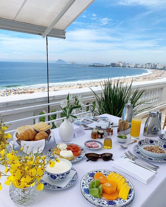 The image features an outdoor breakfast spread with plates of food, including fruit such as bananas, oranges, and apples, along with pastries like croissants and muffins. The table also has various condiments and utensils for use. A vase filled with flowers adds a touch of elegance to the scene. The setting is on an outdoor patio overlooking the ocean, providing a serene backdrop for this meal. The image seems to be related to a post about crypto projects or blockchain technology, as it highlights the importance of preparing for future advancements in technology and the potential impact they could have on various industries.