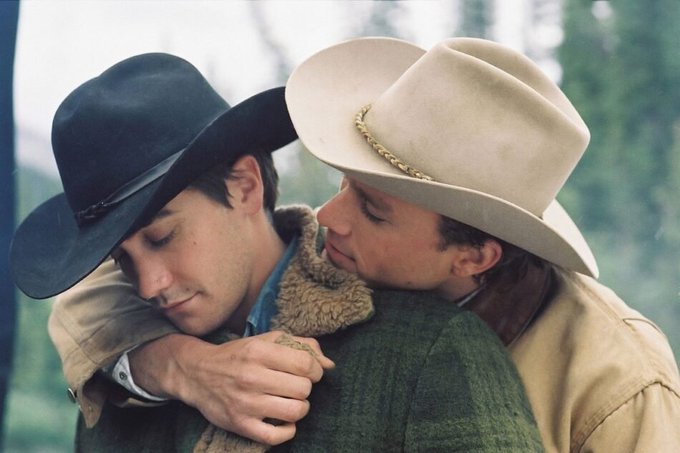 Two men in cowboy hats embrace tenderly, one wearing a black hat and the other a cream-colored one with a braided band, with a small green tattoo visible on the embracing hand. The emotional, intimate moment between the two rugged cowboys ironically contrasts with the post's tongue-in-cheek mention of selling bitcoin, suggesting a bittersweet goodbye or romantic farewell between the pair.