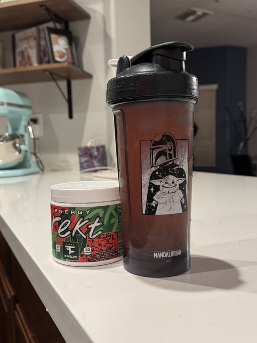 A black Mandalorian-themed shaker bottle and a container of watermelon-flavored G Fuel energy powder sitting on a white kitchen counter.