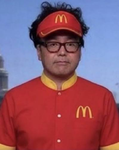 An older man with glasses and messy dark hair wears a red McDonald's uniform shirt and visor, both featuring the yellow "M" logo.