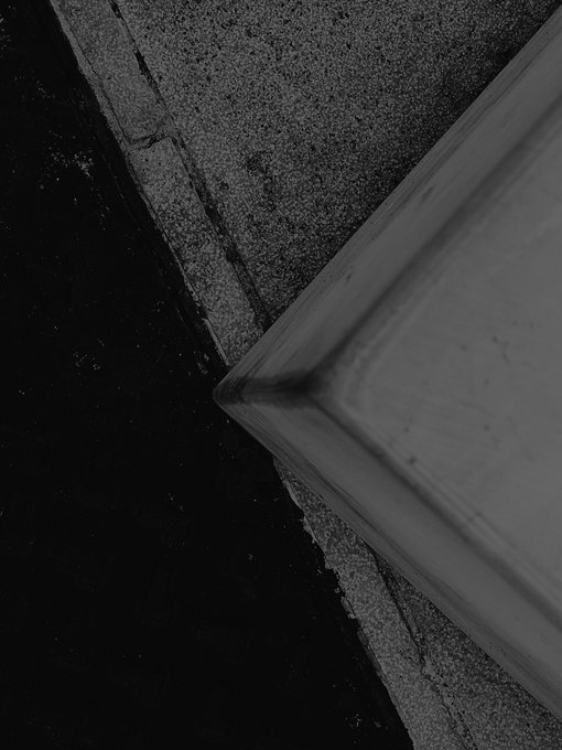 A dark, moody black-and-white photograph capturing a close-up architectural detail where textured concrete meets a smooth wooden surface.