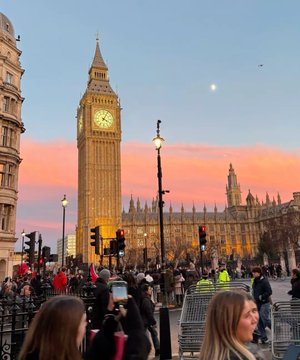 A view of Big Ben and the Houses of Parliament in London at sunset, with crowds of people and police officers gathered in the foreground near traffic lights.