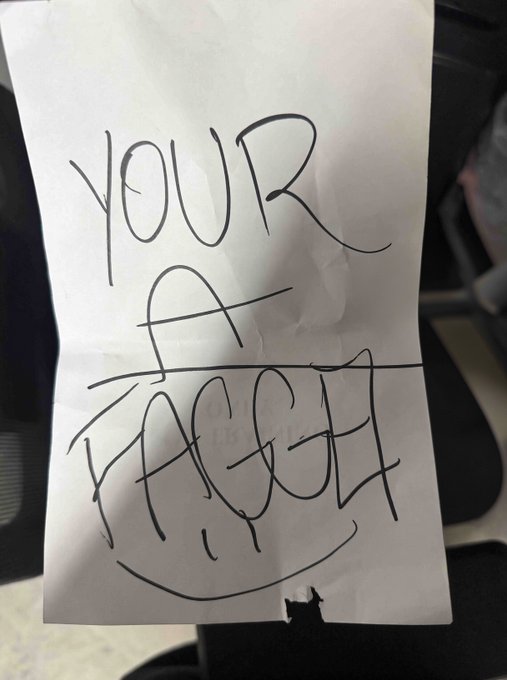 A handwritten note in black marker on white paper reads 'YOUR A FAGGET' (sic).