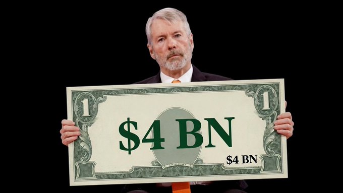 Michael Saylor holds an oversized $4 BN bill representing Strategy's increased cash reserves, funded by MSTR stock sales, Bitcoin sales covering 2.3 years of dividends.