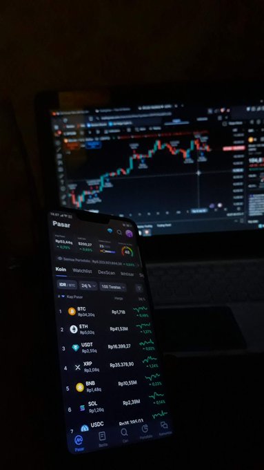 The image features a smartphone displaying various cryptocurrency details, including Bitcoin's value of $5,000 for some reason. The phone is positioned next to an open laptop with a chart showing a fluctuating price range between 2010-2015.