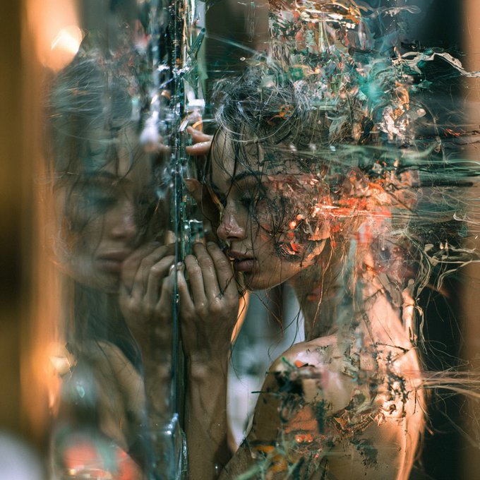 Artistic portrait photograph of a woman with wet hair pressed against a glass surface, featuring complex reflections, water droplets, and warm orange lighting creating a dreamy, fragmented visual effect.