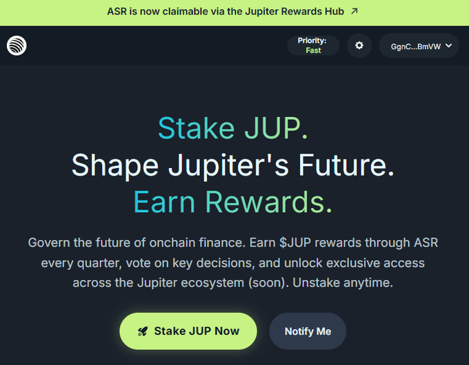 A webpage for Jupiter staking displays the text 'Stake JUP. Shape Jupiter's Future. Earn Rewards.' along with 'ASR is now claimable via the Jupiter Rewards Hub' and buttons for 'Stake JUP Now' and 'Notify Me'.