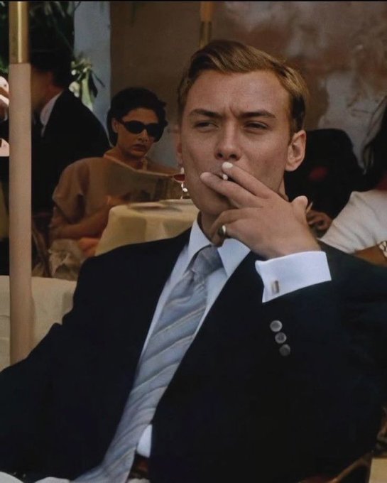 A stylish young man in a dark suit and light blue tie smokes a cigarette at an outdoor café, with a woman in sunglasses seated at a table in the background. The image evokes a vintage, romantic cinematic aesthetic that mirrors the wistful, time-traveling sentiment of the caption about a futuristic Ethereum where Ethereum is quantum-safe, censorship-resistant, and "Lean."