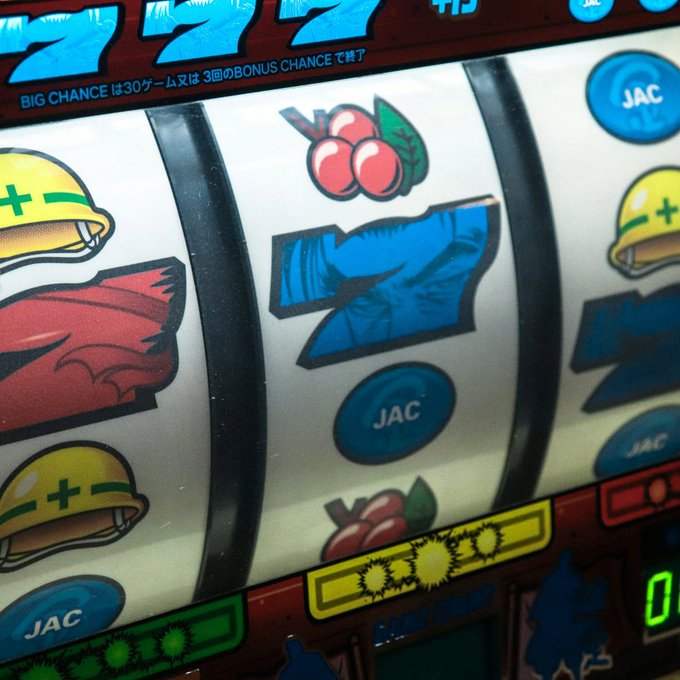 A close-up of a Japanese pachislot or slot machine displaying reels with blue '7' symbols, yellow helmets, red cherries, and 'JAC' markings, along with Japanese text 'BIG CHANCEは30ゲーム又は3回のBONUS CHANCEで終了'.