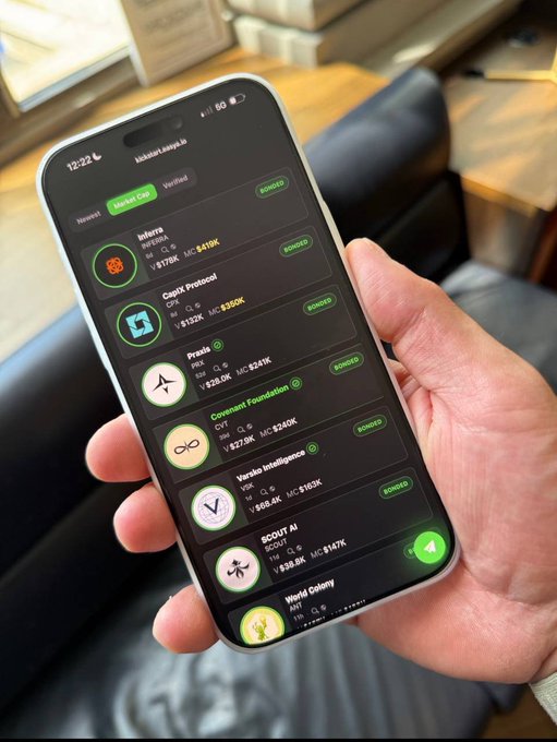 The image shows a person holding up their phone displaying various app icons, including one for Bitcoin. The person's hand is visible above the phone screen as they navigate through the different apps. The background of the image features a couch with a window behind it, suggesting that this scene takes place in a living room or similar indoor setting.