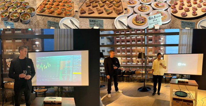 The image is a collage featuring various food items such as pizzas, cakes, and other dishes displayed in a buffet style arrangement. A man can be seen standing near one of the presentations while others are enjoying their meals. Additionally, there's an older man giving a presentation with a projection screen nearby. The post provides context about a party or gathering that includes not only food but also a presentation on the importance of sustainability and the @useTria project for Decibel.
