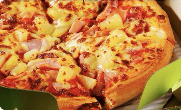 A close-up of a Hawaiian or similar pizza topped with ham and pineapple chunks.