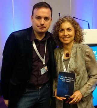 A man and a woman posing together at an event; the woman is holding 'From Big Data to Intelligent Systems: 2016 Edition' by Mariam Kiran.