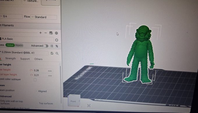 A computer monitor displays 3D printing slicing software with a green model of a gorilla-like figure on the virtual build plate.