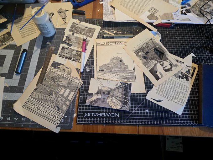 A cluttered workspace with a cutting mat, scattered papers featuring black-and-white illustrations, a pen, glue, and a page showing a concert hall labeled 'KONZERTZAL' and 'NEW BRAUNFELS'.