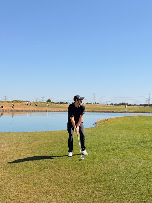 A golfer wearing black attire and a cap prepares to putt on a green next to a water hazard under a clear blue sky.