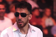 A man with a beard wearing dark sunglasses and a white shirt speaks at what appears to be a press event.