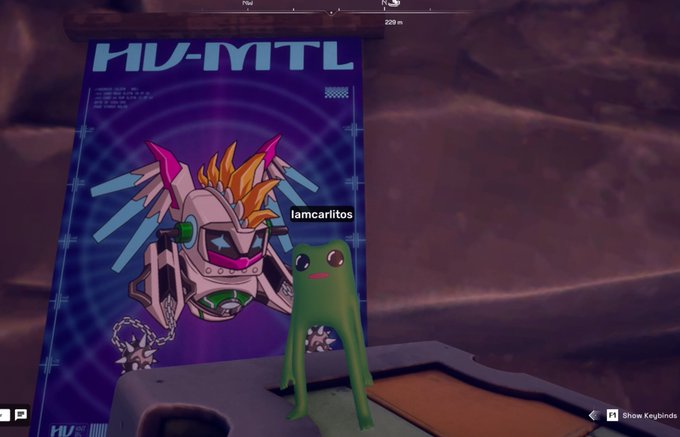A video game screenshot shows a green frog-like character labeled 'lamcarilitos' standing on a surface in front of a blue poster reading 'HU-MTL' featuring a robotic character design.