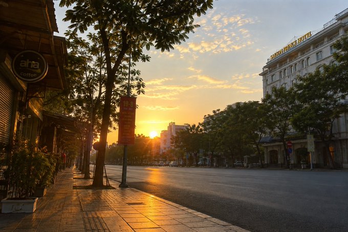 A sunset over a city street in Hanoi, Vietnam, with a "SHERATON HOTEL" sign visible and a "aha coffee" sign on the left.