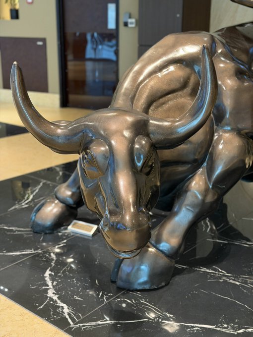 A large bronze-colored statue of a bull with prominent horns, displayed on a polished black marble pedestal in what appears to be a lobby or hallway.