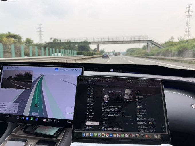 A view from inside a car on a highway shows two laptop screens on the dashboard, with the left displaying a navigation/mapping app (showing "26.5" and "20.0" along with temperature "123°") and the right showing what appears to be a social media or news feed interface. The image captures the beginning of a long road trip from Tianjin toward western China, as the vehicle cruises down an empty highway beneath an overpass, with the laptops set up for entertainment during the 600-kilometer drive.