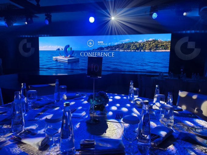 An elegantly set round banquet table is bathed in blue light, with a screen in the background displaying 'CONFERENCE' and 'pepsi VOYAGE' over an image of a tropical island.