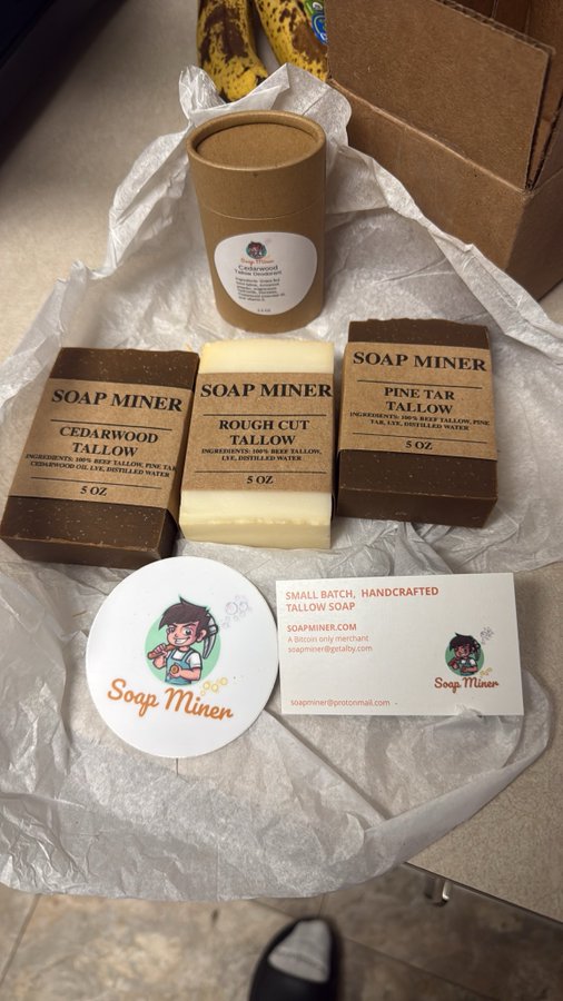 A flat lay displays Soap Miner tallow soap products, including Cedarwood Tallow, Rough Cut Tallow, and Pine Tar Tallow bars (5 oz each), along with a branded card and sticker on tissue paper. The "Bitcoin only" caption ties directly to the brand's printed note reading "A Bitcoin only merchant" on their business card, promoting their acceptance of cryptocurrency as payment.