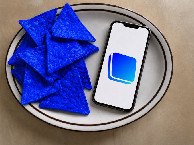 Blue tortilla chips are arranged on a white plate beside a screen displaying the Base app logo. The image visually echoes the post's playful "breakfast" theme by pairing the blue chips—labeled as "bluechip(s)"—with the Base crypto app icon, riffing on crypto slang for top-performing assets.