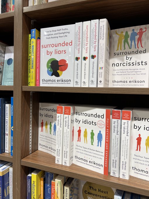 A bookstore display showing multiple copies of books by Thomas Erikson, including "Surrounded by Liars," "Surrounded by Narcissists," and "Surrounded by Idiots," arranged on wooden shelves.
