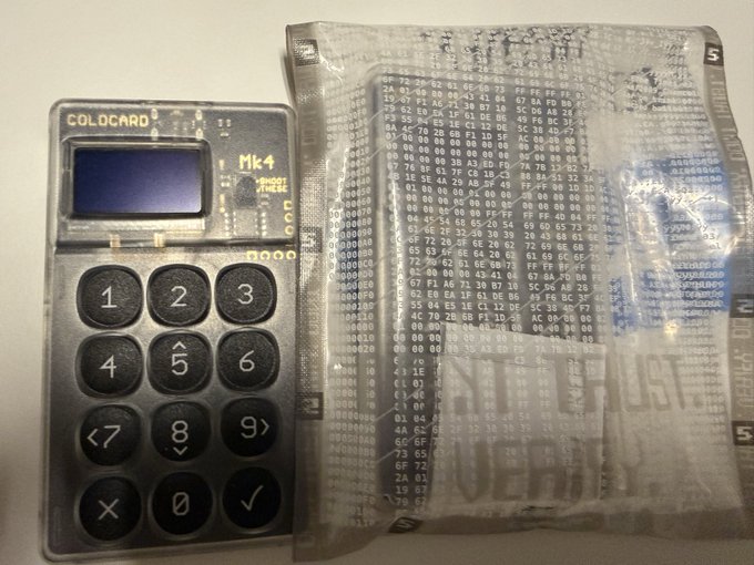 A COLDCARD Mk4 hardware cryptocurrency wallet with a numeric keypad and small screen, photographed next to its anti-tampering holographic security packaging.