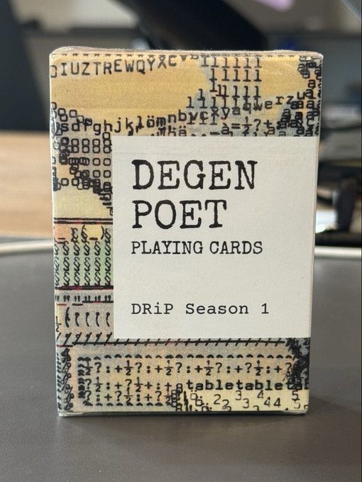 A deck of "DEGEN POET PLAYING CARDS - DRiP Season 1" sitting on a desk, featuring a collage-style wrapper design with typewriter font, numbers, and various characters printed on it.