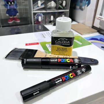 Two Uni Posca markers and a bottle of Winsor & Newton Galeria Acrylic Medium on a desk, with Sonic the Hedgehog figurines visible in the background.