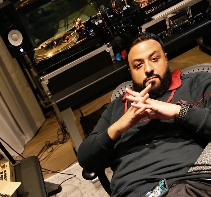 A bearded man in a black hoodie sits with his fingers steepled in a contemplative, judgmental pose in front of DJ equipment labeled "Technics," his piercing stare fitting the "how the coin looks at you after you sold right before it cooked" meme perfectly.