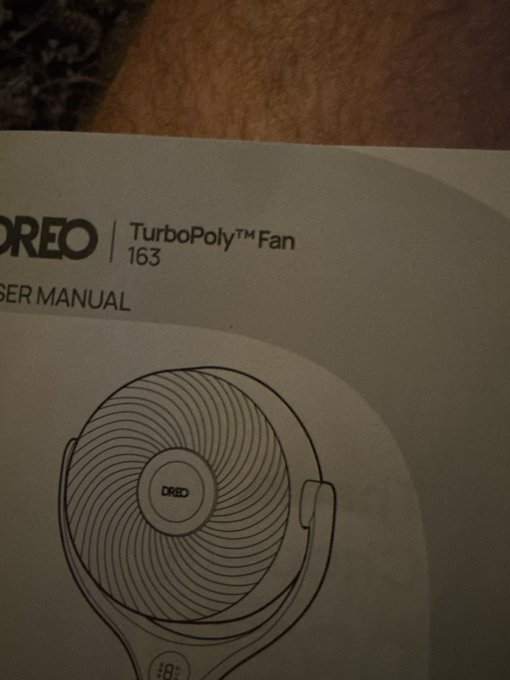 A Dreo TurboPoly Fan 163 user manual resting on a wooden surface, showing an illustration of the fan.