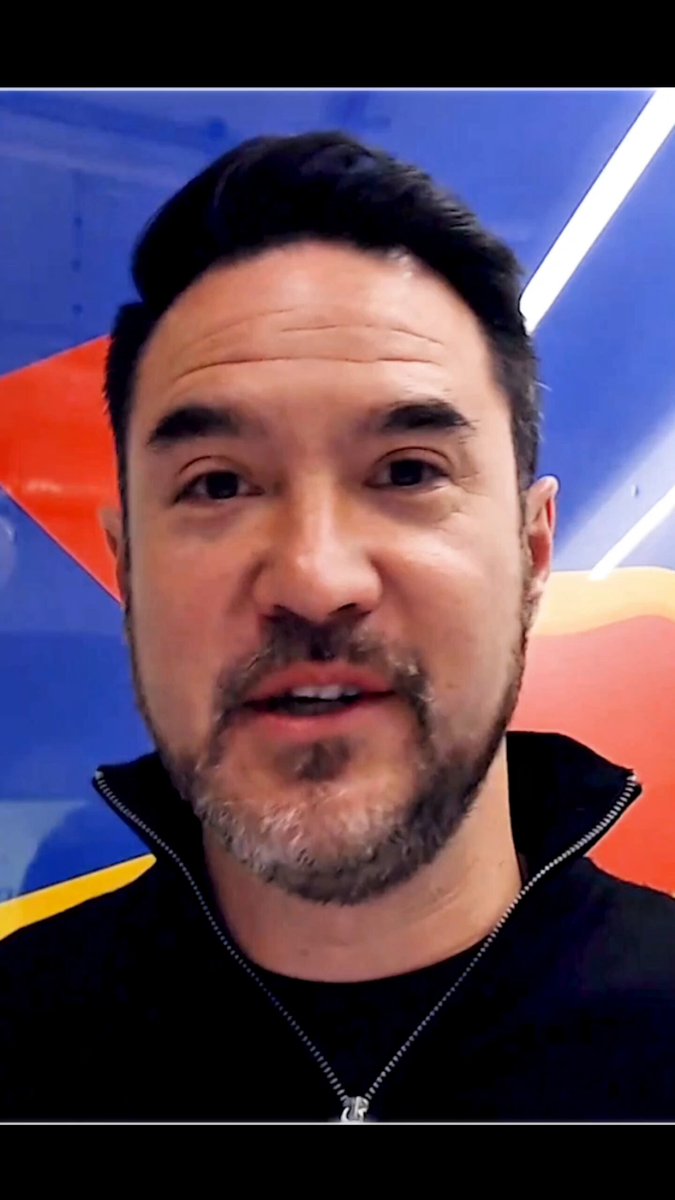 The image features a man with a beard wearing a black shirt, looking directly at the camera while smiling. The background of the photo has a blue and red color scheme, which appears to be part of an art installation or decoration. There are also some text elements in the image that read "AI agents are doing on-chain tasks that humans literally can'T". This suggests that there might be a connection between the man's facial expression and the AI agents performing on-chain tasks.