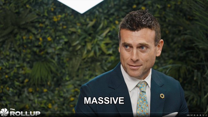 The image shows a man in a dark suit with a floral tie, speaking in front of a green plant wall backdrop, with the caption "MASSIVE" displayed below him and "The Rollup" logo in the bottom corner. The caption directly emphasizes the massive opportunity being discussed for Chainlink ($LINK), with the interviewee likely elaborating on the project's potential in the blockchain space.