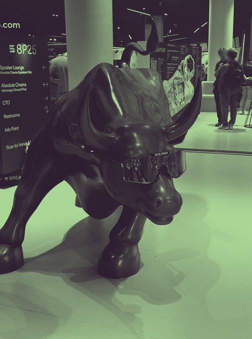 A dark, glossy bull statue wearing Burberry sunglasses is displayed in an indoor venue with greenish lighting, with a directory sign visible to the left.