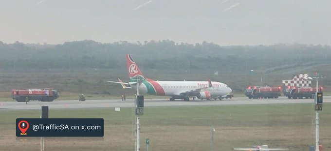 An airplane on a runway surrounded by red fire trucks, with a watermark reading '@TrafficSA on x.com' in the lower left corner.