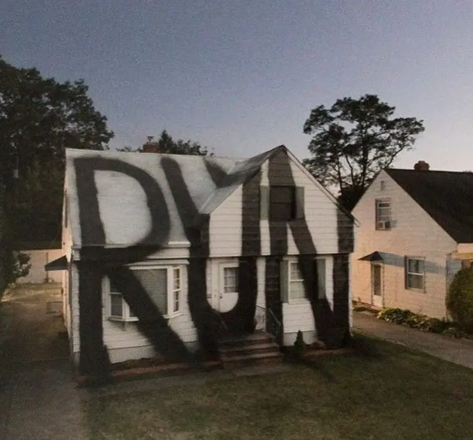 A drone photograph of a white suburban house with "DUNKIN" painted in massive black letters across its entire facade as an apparent prank or stunt.