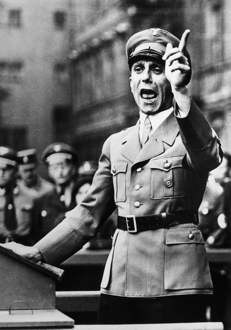 A black-and-white historical photo showing a uniformed officer giving an animated speech with his fist raised.