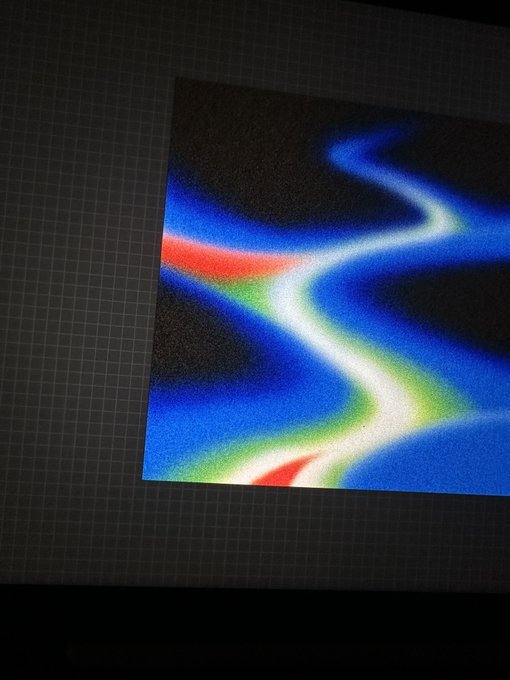 A photograph of a screen displaying wavy lines of blue, red, green, and white colors on a dark grid background.